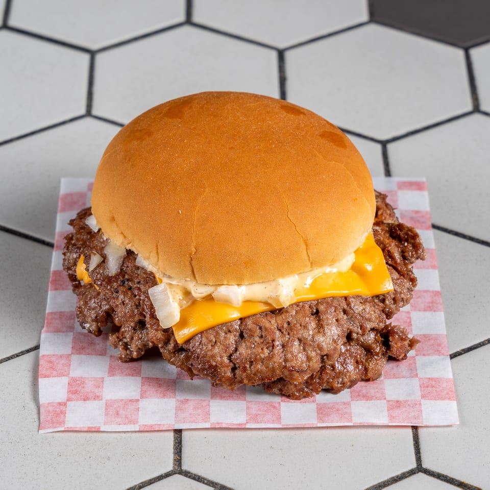 Smashed double cheeseburger with melted cheese, diced onions, and creamy sauce on a golden bun.