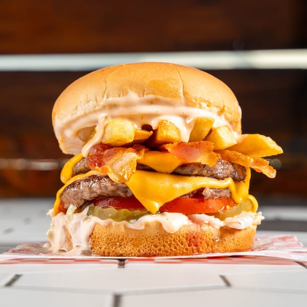 Double cheeseburger topped with bacon, melted cheese, pickles, tomatoes, special sauce, and fries on a bun.