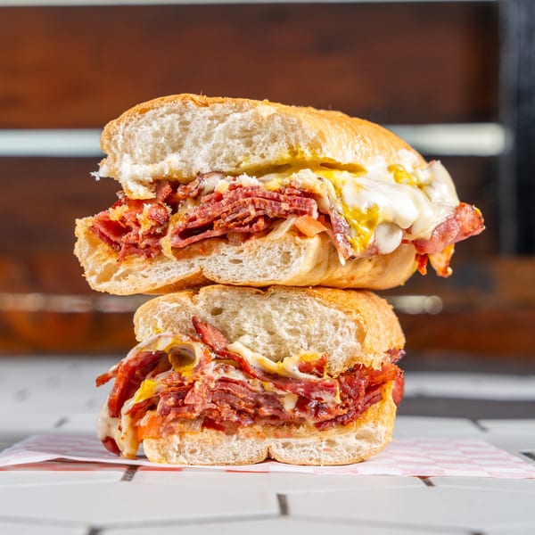 Stacked halves of a deli sandwich overflowing with sliced meat, melted cheese, and mustard.