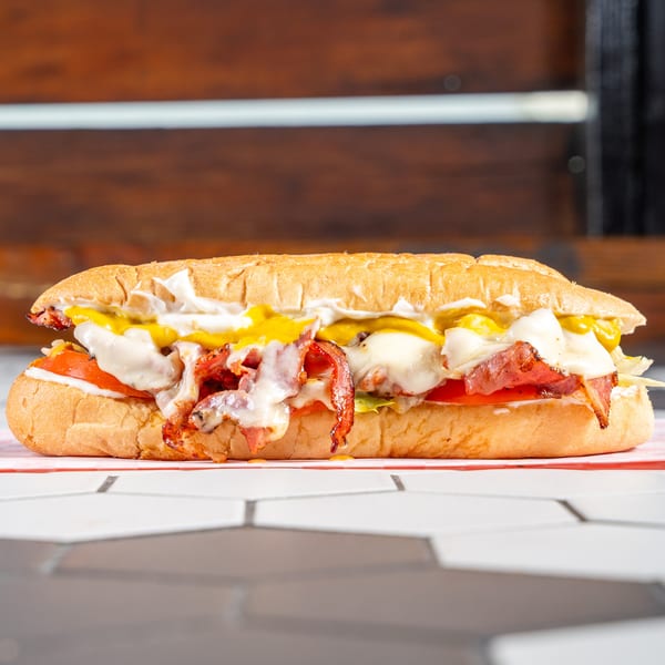 Loaded sub sandwich with crispy bacon, melted cheese, tomatoes, lettuce, mustard, and mayo.