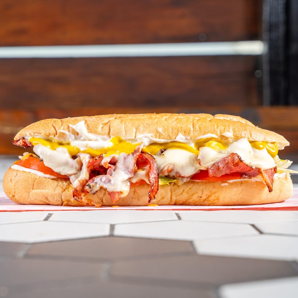 Loaded sub sandwich with crispy bacon, melted cheese, tomatoes, lettuce, mustard, and mayo.