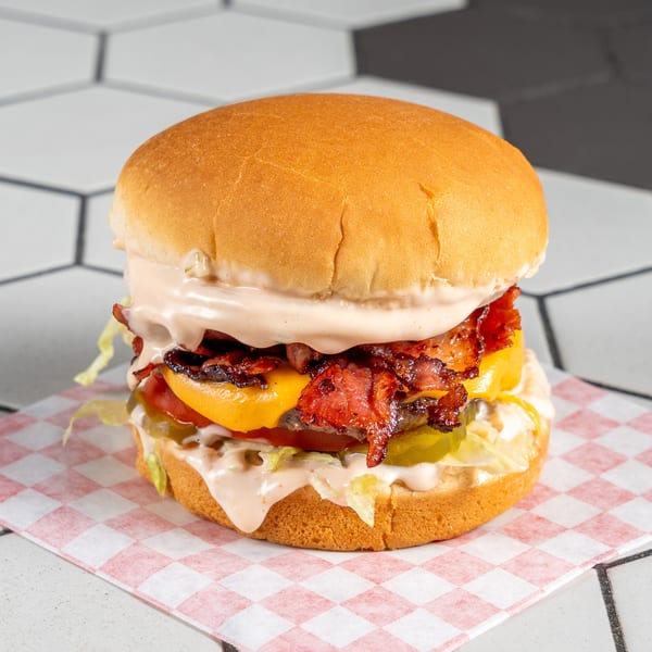 Juicy bacon cheeseburger with lettuce, tomato, pickles, and creamy sauce on a checkered paper.
