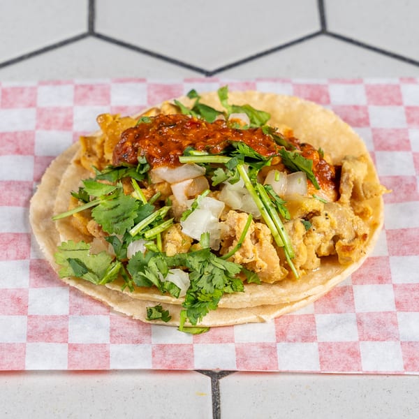 Scrambled egg taco topped with red salsa, fresh cilantro, and diced white onions.