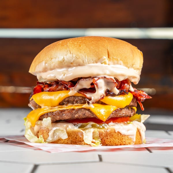 Double cheeseburger stacked with bacon, lettuce, pickles, tomatoes, and creamy sauce on a bun.
