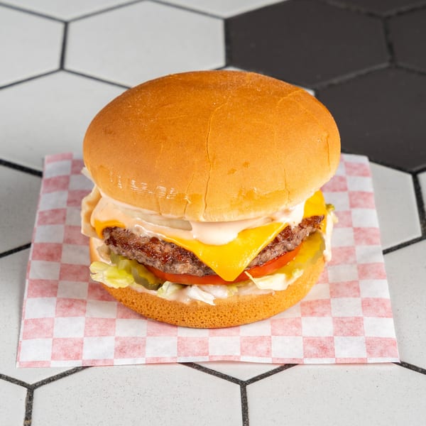 Classic cheeseburger with melted cheese, lettuce, tomato, pickles, and sauce on checkered paper.
