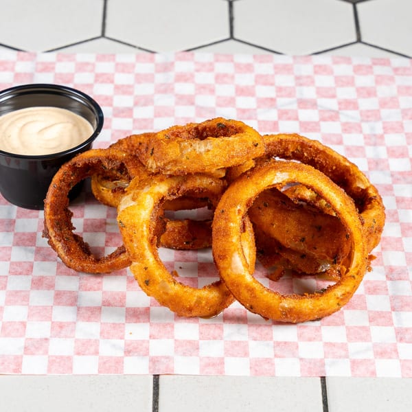 Golden-brown onion rings with a side of creamy dipping sauce on checkered paper.