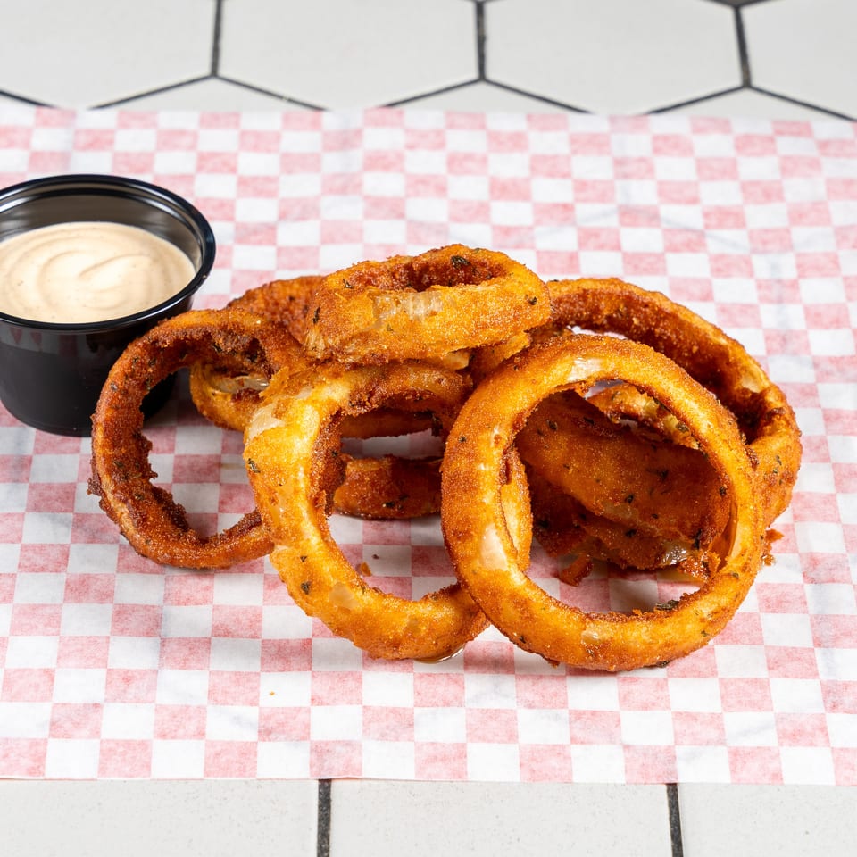 Golden-brown onion rings with a side of creamy dipping sauce on checkered paper.