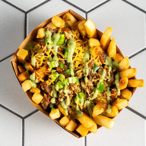 Overhead view of loaded fries with chili, cheese, green sauce, and peppers in a brown tray.