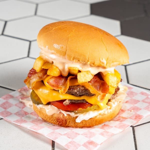 Double cheeseburger with bacon, fries, lettuce, tomato, and sauce on checkered paper.