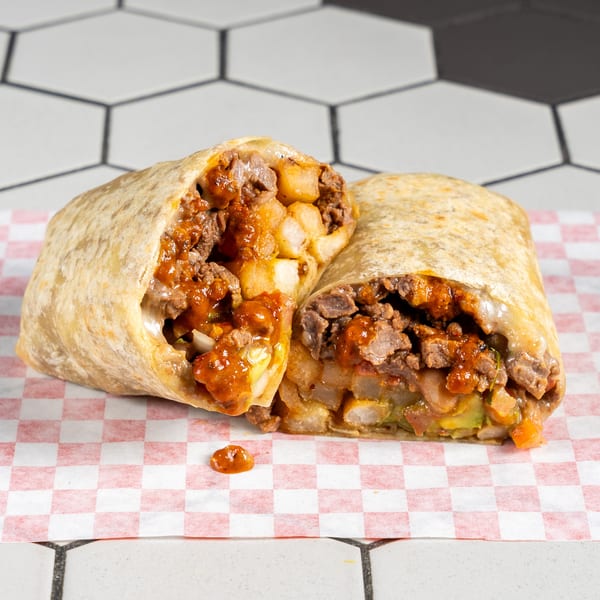 Burrito cut in half, revealing steak, fries, and spicy sauce on checkered paper.